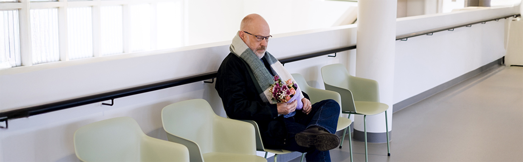 Mies istuu tuolilla kukkakimppu sylissä.