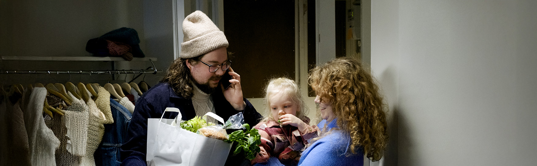 Kaksi aikuista ja pieni lapsi eteisessä. Lapsi on toisen aikuisen sylissä.